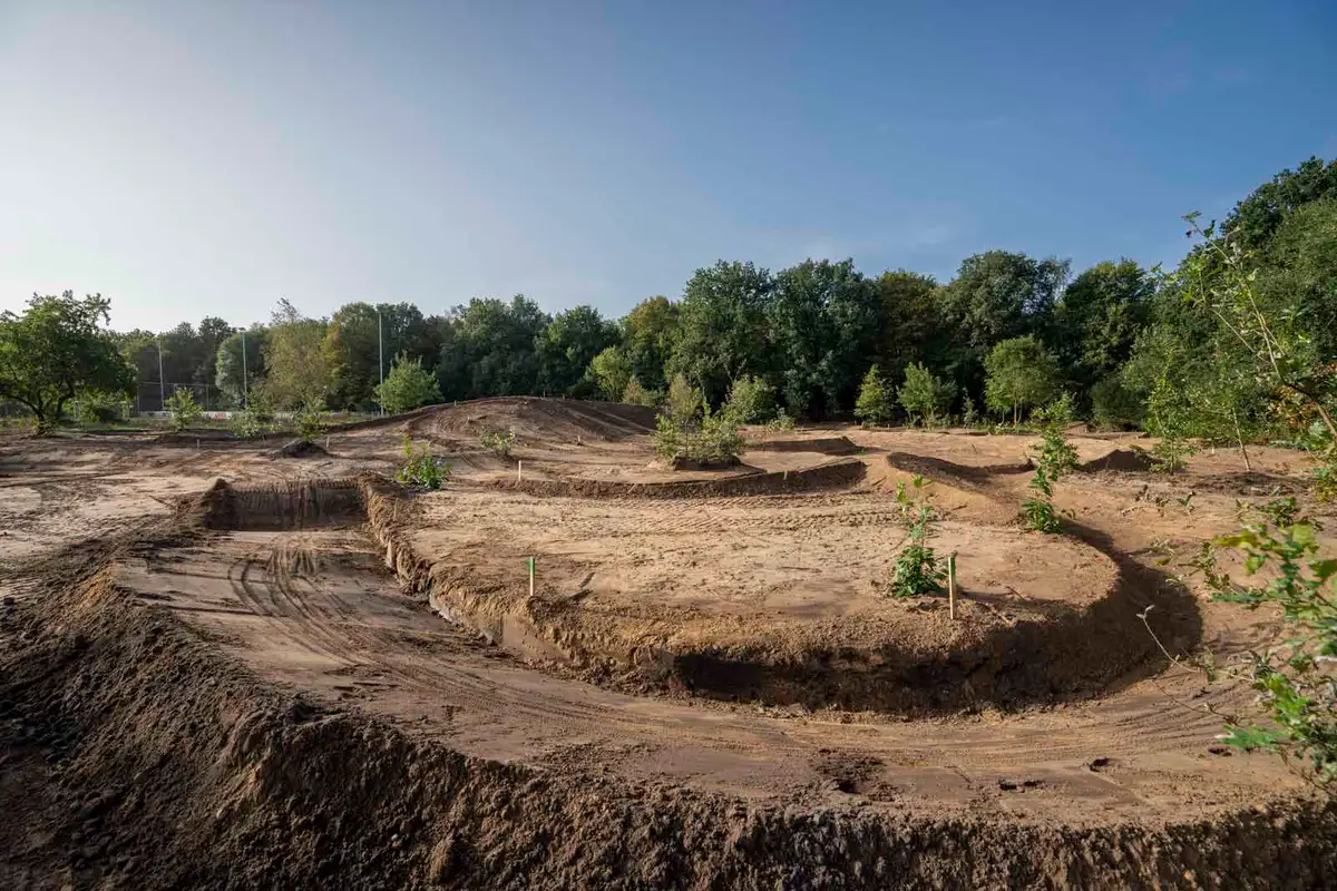 De aarden bochten van het bikepark in aanleg, met bos op de achtergrond
