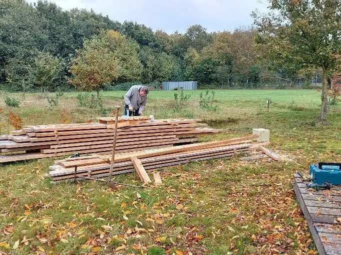 Een vrijwilliger bij stapels hout op het bikepark voor de bouw van nieuwe toestellen